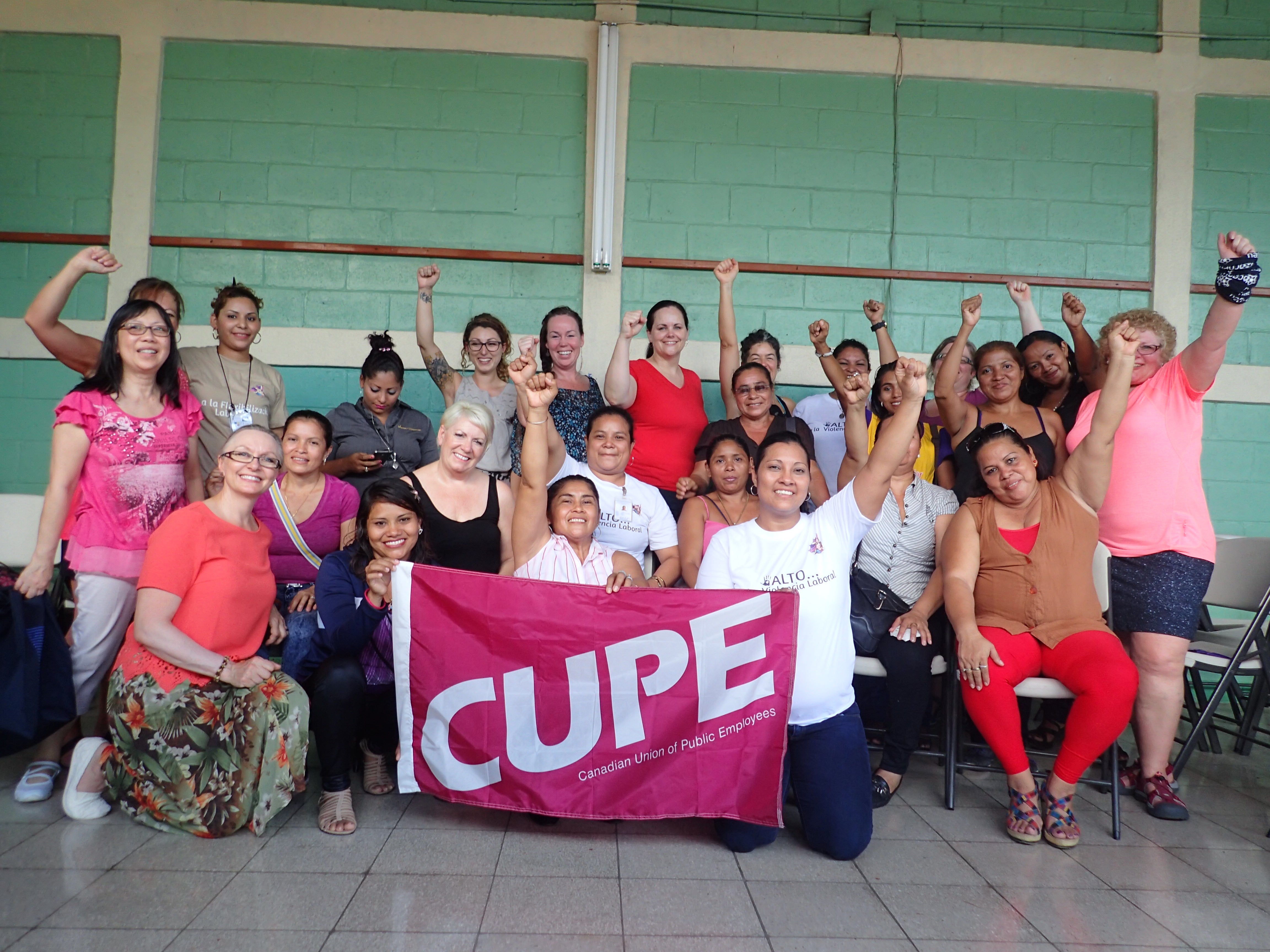 Group of women with raised fists holding a pink CUPE flag