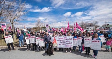 Group of people holding holding CUPE signs and flags, with a black Newfoundland do in the centre.