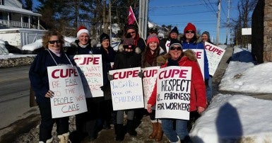 Group of men and women in winter clothing, wearing CUPE strike signs with slogans