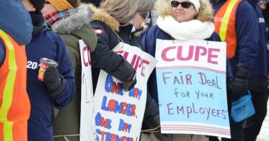 Crowd of women in winter coats and carrying CUPE strike signs