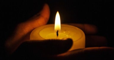 Two hands holding a small lit candle with darkness in the background