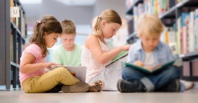 Group of four children sitting on a library floor and reading books