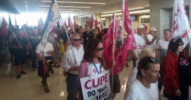 A crowd of mena and women with placards and flags march into a public building