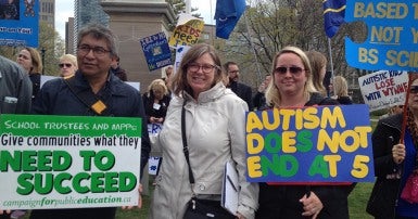 Two women and one man hold autism activism signs at a protest
