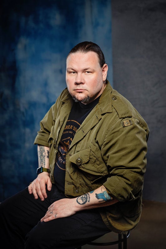 A man in a green jacket sitting in front of a dark blue background