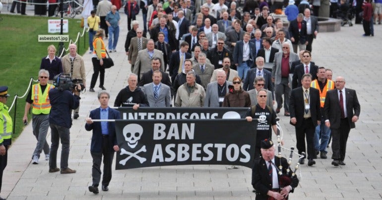 Photo of a 2010 CUPE rally against asbestos with men on the front lines carrying banners asking for a ban on asbestos.