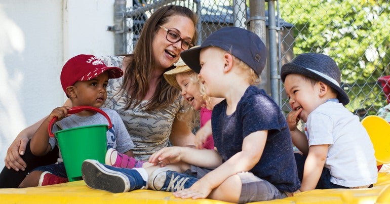 Four pre-school aged children laughing with a woman in glasses