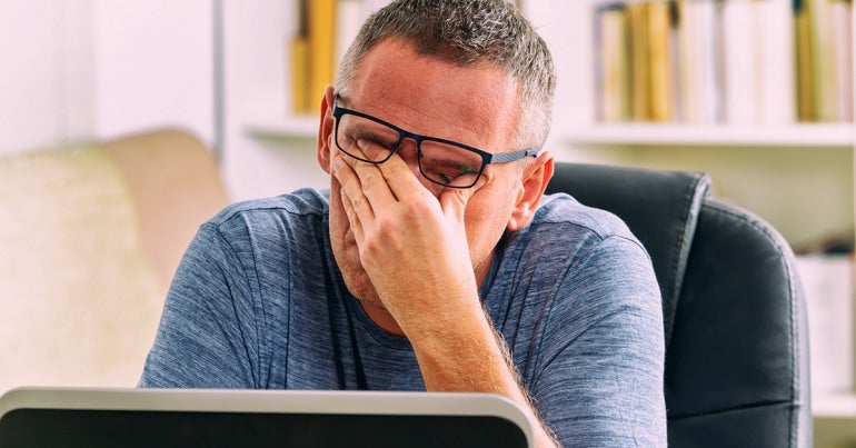 Close up of man with short salt and pepper hair and glasses, rubbing his eyes