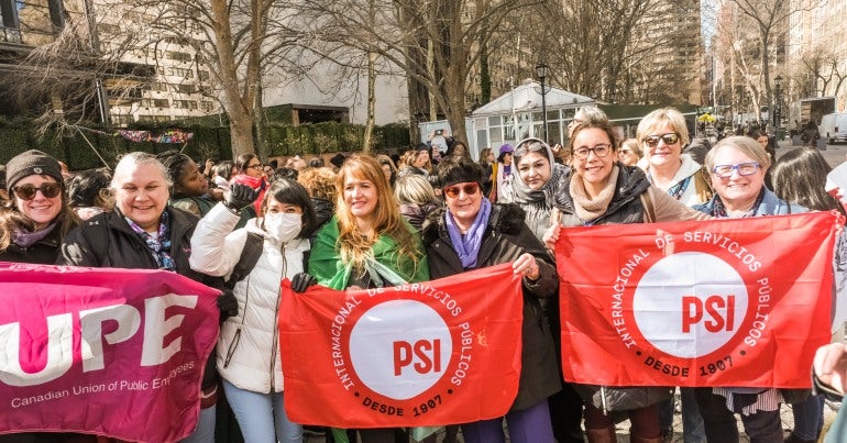 A group of women holding flags with a crowd behind them