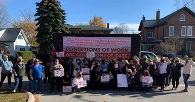 Group of workers wearing masks and holding signs that say "Conditions of work are conditions of care"