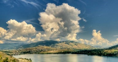 Image of lake surrounded by mountains in summer with dramatic cloud 