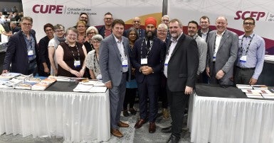 A group of people including Mark Hancock, Charles Fleury and Jagmeet Singh standing in front of a backdrop that says CUPE/SCFP