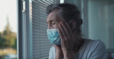 Woman in long term care facility wearing mask looking out window