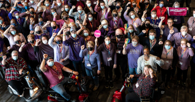 Group of CUPE members in purple shirts host up CUPE signs with fists raised.