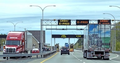 Cars and trucks on a toll road with signs that say Cash/E-Pass