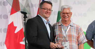 Two men standing on stage in front of a Canadian flag holding an award