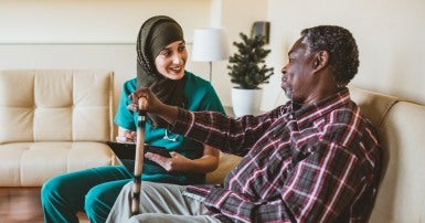 Young continuing care assistant with a clipboard speaking to older man holding a cane