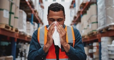 Young Black warehouse worker blowing his nose