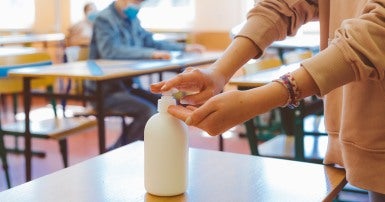 Student using hand sanitizer in classroom with other students