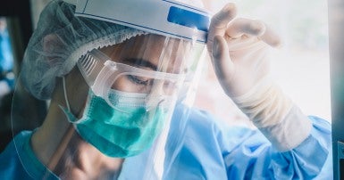 Tired healthcare worker wearing scrubs, a mask, goggles, and shield 