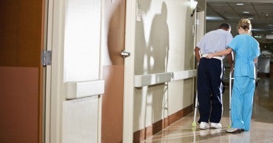 Woman in scrubs assisting an elderly man with a walker 