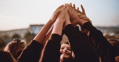 Soft focus image of a small group of women with their arms raised, touching hands