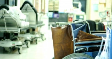 Photo of a hospital room with empty wheelchairs in the foreground and empty gurneys in the background.