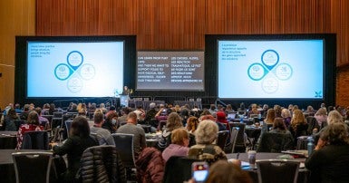 Photo of a restorative practices presentation in front of many members in a conference hall.