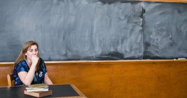 Photo of worried female teacher at desk in front of blank blackboard