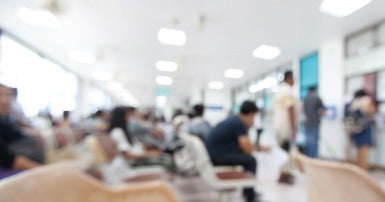 Blurry photo of people sitting and standing in a bright hospital waiting room