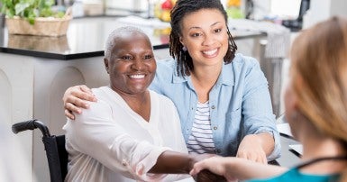 Woman using a wheelchair, next to a second woman, shaking hands with a third.