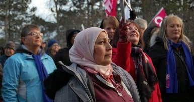 Woman in a light coloured head scarf and winter coat in a crowd of people