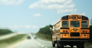 A school bus traveling down a highway. Photographed with a tilt-shift lens.