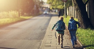 Two school kids running down a sidewalk