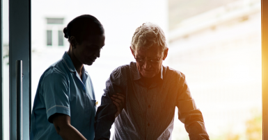 Care aid standing beside elder man who leans on her