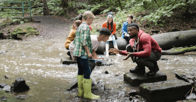 Students listen to instructor by a water stream in a forest