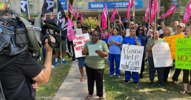 Person speaking at a rally in front of news cameras