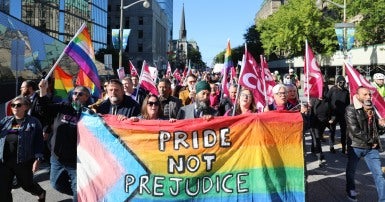 People holding a banner that reads Pride not Prejudice with a crowd marching behind them