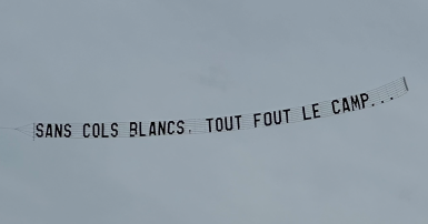 Plane flying a banner that reads sans cols blancs, tout fout le camp