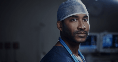 Man wearing scrubs and a surgical cap in a darkened hospital room