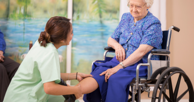 Continuing care assistant kneels and rubs the leg of a senior woman in a wheelchair