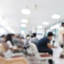 Blurry photo of people sitting and standing in a bright hospital waiting room
