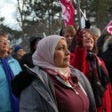 Woman in a light coloured head scarf and winter coat in a crowd of people