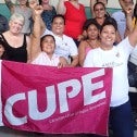 Group of women with raised fists holding a pink CUPE flag