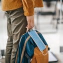 A person holding a backpack and a paper mask from the legs down.