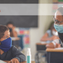 Web banner. Image: Teacher talking to young student at his desk. Both are wearing a face mask. CUPE NS logo.