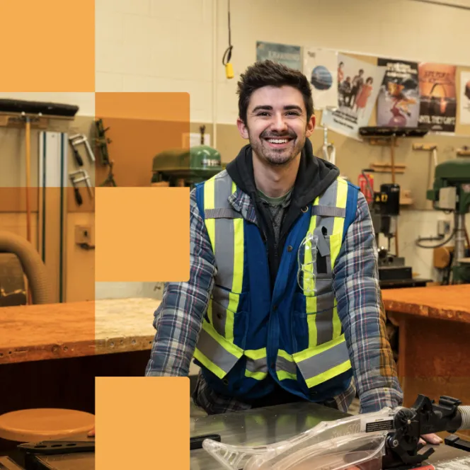 Person smiling in a workshop, wearing a safety vest.