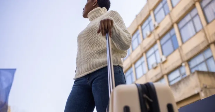 A woman looking into the sky, holding a suitcase handle