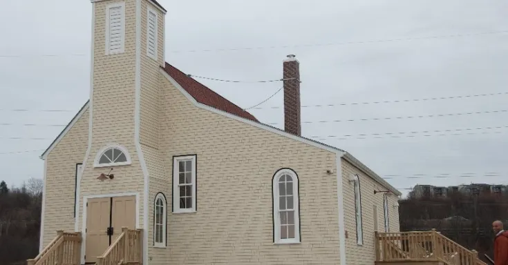Beige coloured chruch with a red roof, a bell tower and arched windows