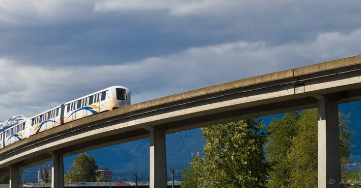 Image of Vancouver SkyTrain, elevated light rapid transit train and track with mountains and blue sky in the background.